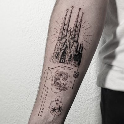 Un tatuaje en blanco y negro en el antebrazo de una persona realizado por Estudio de Tattoos presenta la basílica de la Sagrada Familia, diseños geométricos, una ola abstracta, una flor circular, un indicador de punto de interés y la palabra "BARCELONA". El torso y el brazo de la persona son parcialmente visibles sobre un fondo liso.